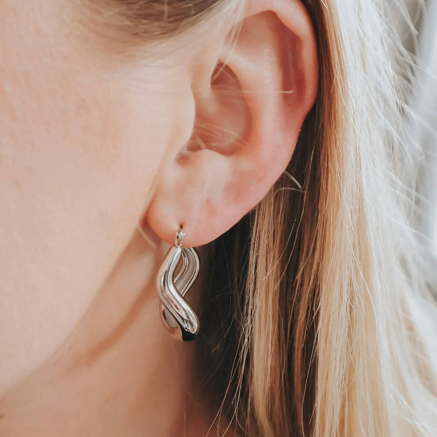 Close-up of an ear wearing a silver earring with blonde hair.
