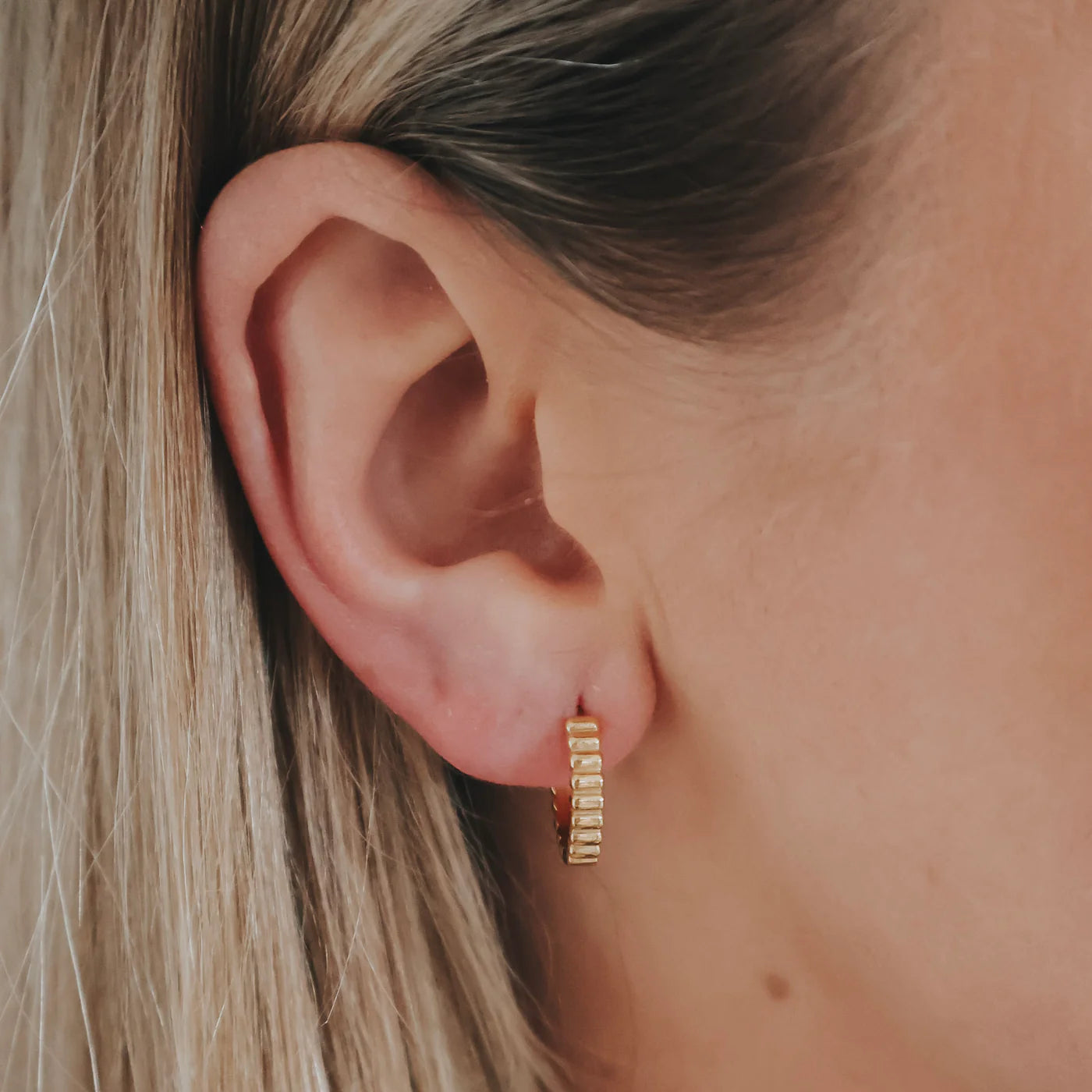 Gold hoop earring worn by a person with blonde hair.