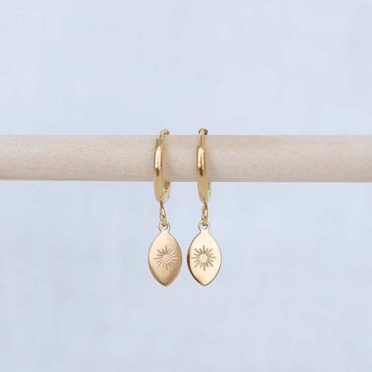 Gold hoop earrings with teardrop-shaped charms on a light gray background